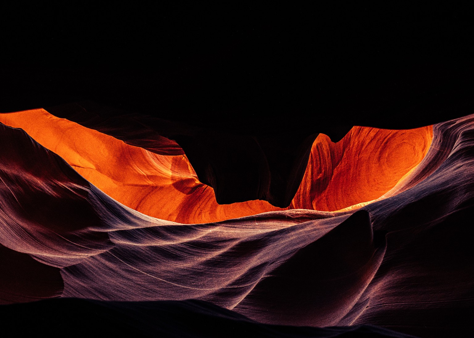 Reflected light illuminates an orange ribbon of sandstone above flowing, purple-toned curves. Arizona, USA.